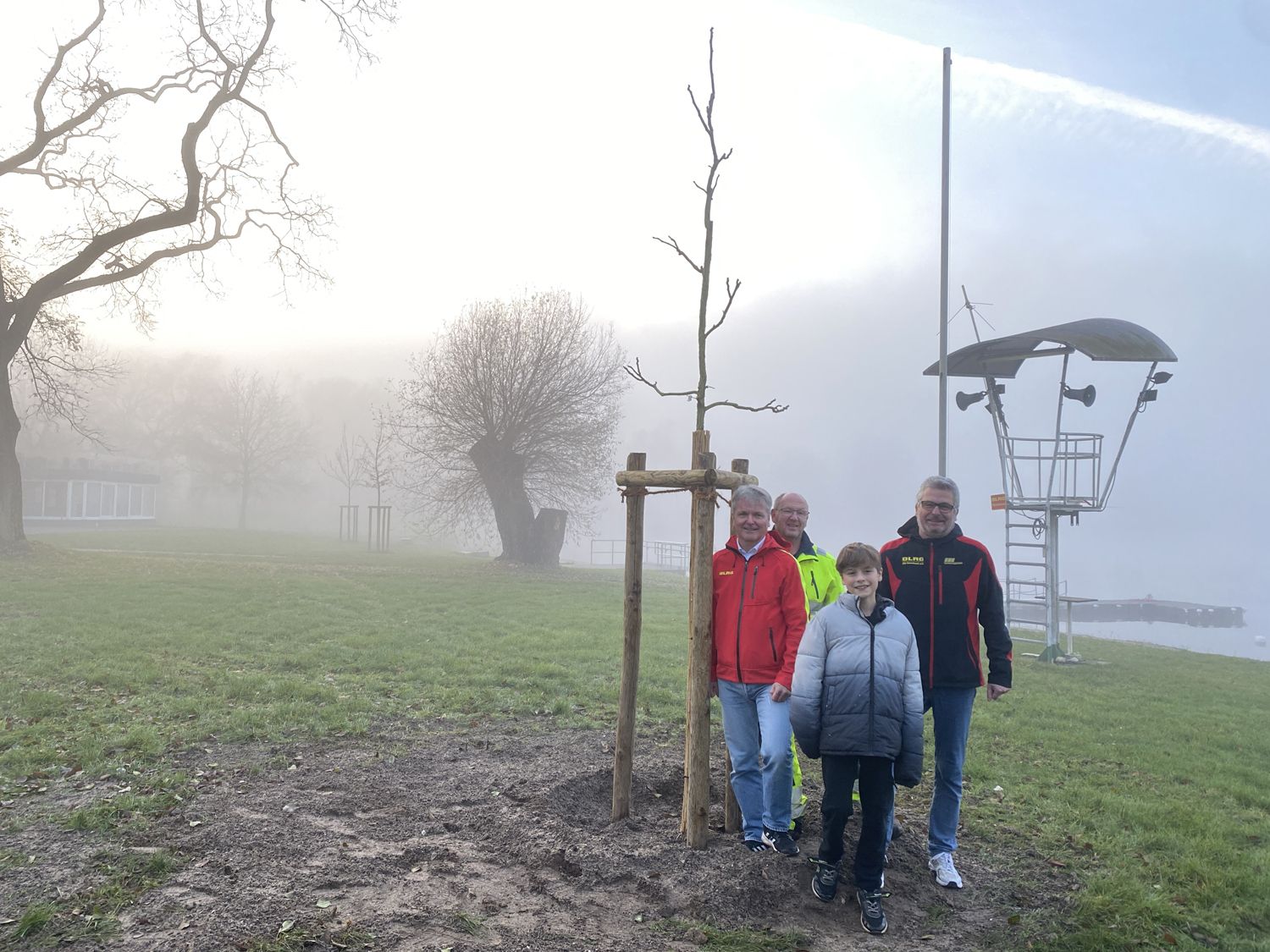 Neu gepflanzter Baum auf dem Wiesensee-Gelaende und Mitglieder der DLRG