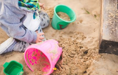 Kind spielt in der Sandkiste mit bunten Eimern und Förmchen